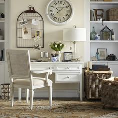 a white desk topped with a chair next to a lamp and a wall mounted clock