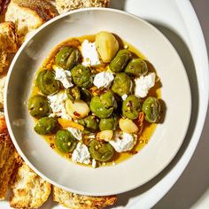 a white bowl filled with olives and feta cheese on top of toasted bread