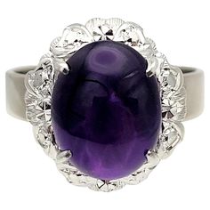 Ring Size 6.75 Indulge in the timeless allure of this stunning cabochon amethyst solitaire cocktail ring. Elegantly designed, this incredible 10 karat white gold ring showcases a high profile 4.00 carat oval cabochon amethyst gemstone that captivates with its vibrant purple hue. Expertly prong set above two layers of delicately crafted heart motifs, the mesmerizing gemstone radiates romance and sophistication. The plain and polished white gold band completes the piece, allowing the vibrant ameth Gold Cocktail Ring, Gold Cocktail, Vibrant Purple, White Gold Band, Oval Cabochon, Amethyst Gemstone, Gold Band, Cocktail Rings, White Gold Rings