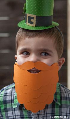 a young boy wearing a green hat with a fake beard and mustache on top of his head