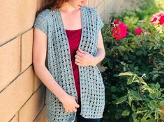 a woman leaning against a wall wearing a blue crochet cardigan