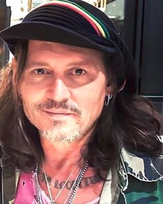 a man with long hair wearing a black hat and green camo jacket is looking at the camera