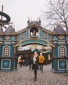 a woman standing in front of a blue and gold building with people walking around it