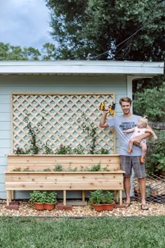 a man holding two children in front of a garden bench with plants growing on it