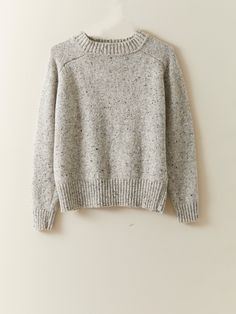 a gray sweater hanging on a wall with a white hanger in front of it