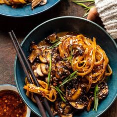 a bowl filled with noodles and mushrooms on top of a wooden table next to chopsticks