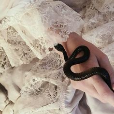 a hand holding a snake on top of a white lace covered bed spread with lacy material