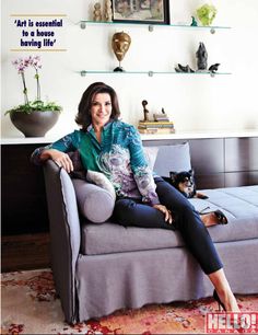 a woman sitting on top of a gray couch next to a black and white dog