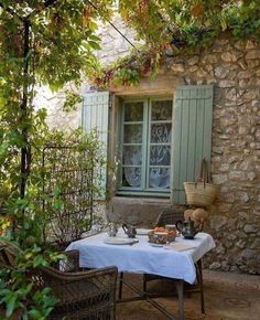 an outdoor table with food on it in front of a stone wall and green shutters