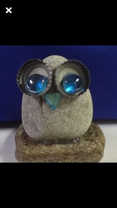 an owl figurine with blue eyes sitting on top of a stone slab in front of a blue wall