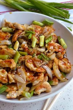 a white bowl filled with chicken and vegetables on top of a table next to chopsticks