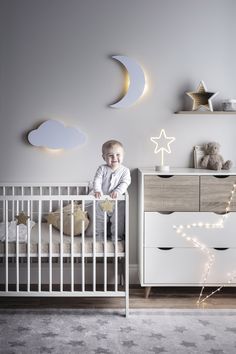 a baby is standing in his crib next to the moon and stars on the wall