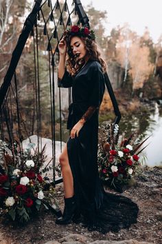 a woman wearing a black dress and flower crown sitting on a swing with flowers in her hair