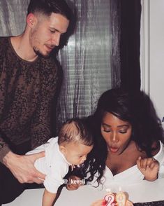 a man and woman are blowing out candles on a cake with a baby in the foreground