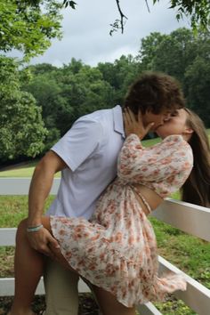 a man kissing a woman on the cheek in front of a white fence with trees