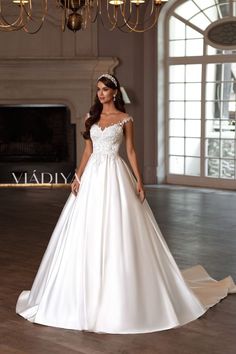 a woman in a white wedding dress standing on a wooden floor next to a chandelier