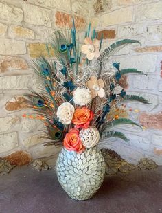 a vase filled with flowers and feathers on top of a stone floor next to a brick wall