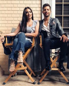 a man and woman sitting next to each other on chairs in front of a brick wall