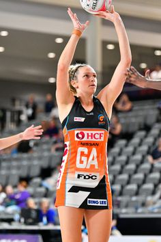 a woman in an orange and black uniform reaching up to hit a volleyball with her hands