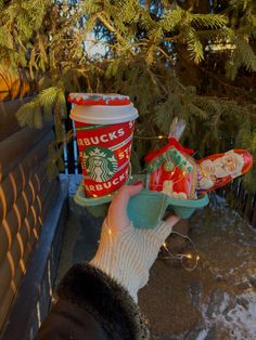 a person holding a starbucks cup and christmas cookies in their hands, next to a tree