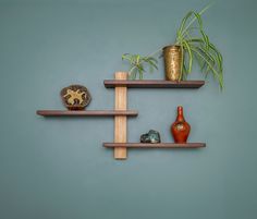 two wooden shelves with plants and vases on them against a gray wall in the corner