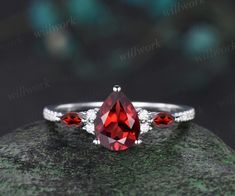 a ring with three pear shaped red stones on top and two diamonds around the band