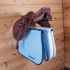 two saddles hanging from the side of a wooden wall