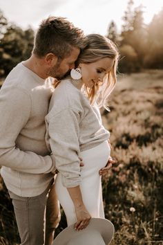 a pregnant couple cuddles in the grass while holding each other's back