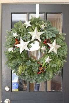 a christmas wreath with white stars and evergreen leaves on the front door, hanging from a black wooden door