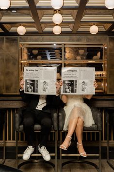 two people sitting on chairs holding up newspapers in front of their faces as they look at each other