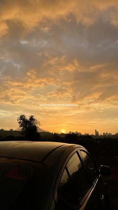 a car parked in front of a sunset with the sun setting behind it and some clouds