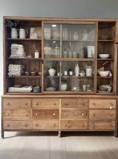 an old wooden cabinet with glass doors and shelves filled with dishes, cups, and vases