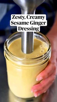 a person holding a spoon over a jar with some liquid in it and the words zesty, creamy sesame ginger dressing