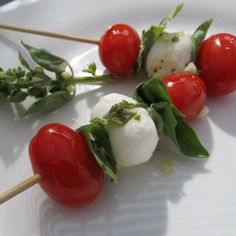 three skewers of mozzarella and cherry tomatoes on a white plate with green leaves