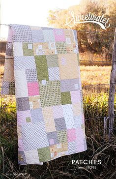 a patchwork quilt hanging on a fence in front of a field with grass and trees