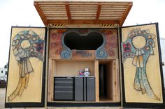 an outdoor kitchen with two painted murals on the wall and cupboards in the doorway