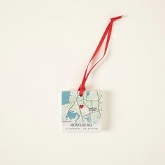 a map ornament hanging from a red string on a white wall with a red ribbon