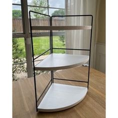 three tiered shelf in front of a window with a wooden floor and white curtains