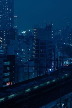 the city skyline is lit up at night with high rise buildings and train tracks in the foreground