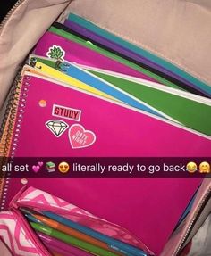 a pink backpack filled with lots of different colored papers and pencils on top of it