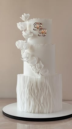 a three tiered white wedding cake with ruffles and gold rings on top