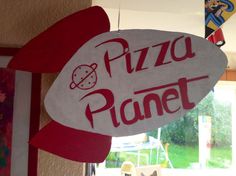 a pizza planet sign hanging from the side of a wall in front of a window