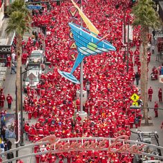 a large group of people in red shirts are walking down the street with one person flying a kite