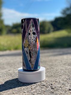 a painted cup sitting on top of a white stand in the middle of a road