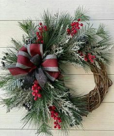 a christmas wreath with red berries, pine needles and silver ribbon on a white wooden background