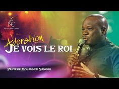 a man holding a microphone in front of a stage with bright lights and the words je vos le roi on it