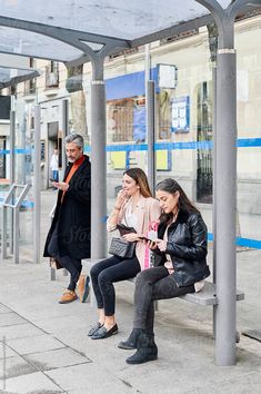 two women sitting on a bench in front of a bus stop by an older man