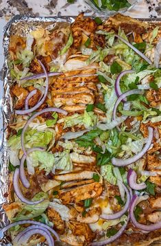 a pizza with chicken, lettuce and onions on it sitting on top of tin foil