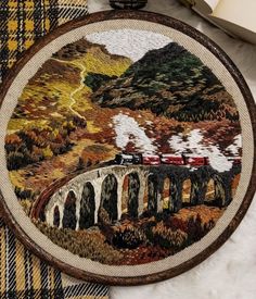 a cross stitched picture of a train crossing a bridge in the mountains with trees