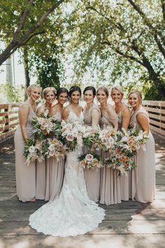 a group of women standing next to each other on a wooden bridge holding bouquets